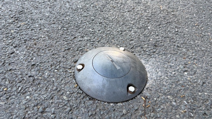 Auf dem Asphalt ist eine kleine runde Scheibe eingelassen