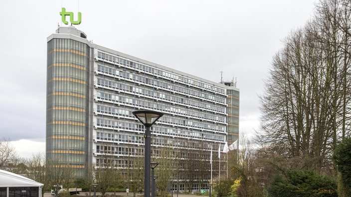 Die Technische Universität Dortmund: ein mehrstöckiges Gebäude mit vielen Fenstern, auf dem Turm links thront das hellgrüne Logo der Universität. Ein hellgrünes "tu".