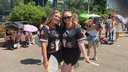 Zwei junge Frauen posieren mit Bad-Bunny-Trikots und Fächern vor einer Warteschlange.