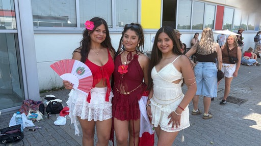 Drei junge Frauen posieren zusammen in kurzen Outfits.