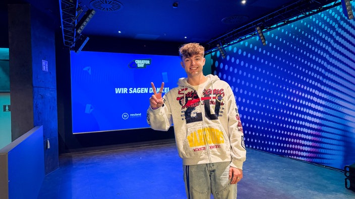 Ein junger Mann in grauer Sweatshirt-Jacke zeigt mit seinen Fingern Peace