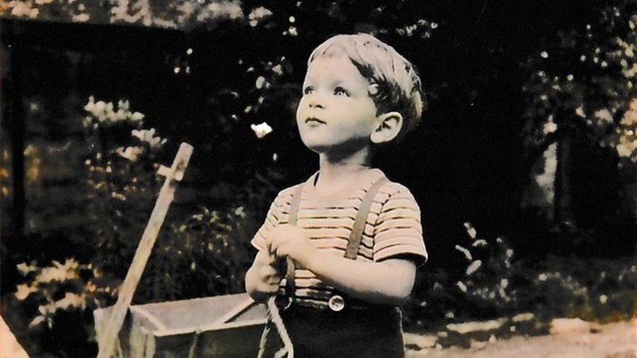 Eine schwarz-weiß Aufnahme von einem kleinen Jungen, der in einem Garten steht.