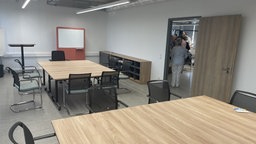 Ein moderner Seminarraum, in der Mitte stehen zwei Tische umringt von Stühlen und einem Whiteboard an der Wand.