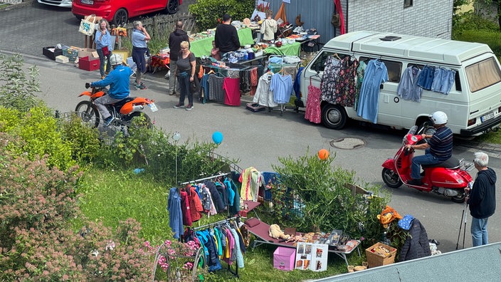 Eine Straße mit mehreren Flohmarktständen, unter anderem im Garten und aus dem Wohnmobil heraus