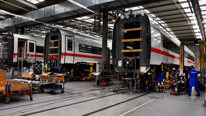 Weiß-rote ICE-Waggons stehen im Aufbau in der hell erleuchteten Produktionshalle im Siemens Mobility Werk in Krefeld