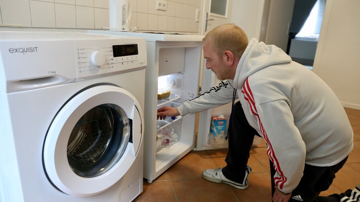 Ein Mann greift in den Kühlschrank, links daneben steht eine Waschmaschine