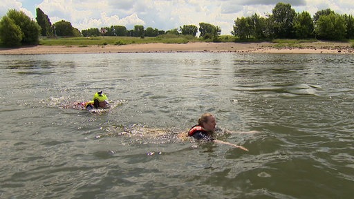 Reporterin Annika Müller und ein Strömungsretter der DLRG schwimmen im Rhein gegen die Strömung.
