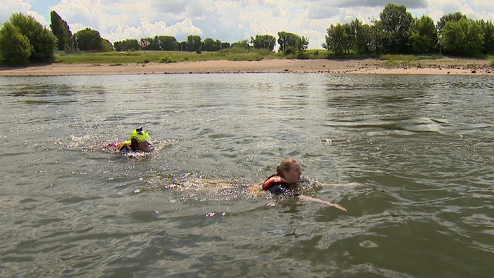 Reporterin Annika Müller und ein Strömungsretter der DLRG schwimmen im Rhein gegen die Strömung.