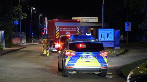 Zwei Polizeiwagen und ein Fahrzeug vom Katastrophenschutz passieren den Südeingang des Uniklinikums Düsseldorf