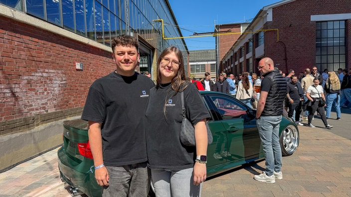 Zwei Besucher beim Tuning-Treffen "Ultrace" in Düsseldorf vor einem grünen Auto 