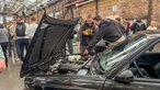 Mehrere Menschen stehten über dem geöffneten Motorraum eines Autos