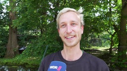 Ein junger Mann mit blonden Haaren schaut in die Kamera.