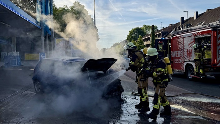 Feuerwehrleute löschen den qualmenden Motorraum eines Autos neben einer Tankstelle in Essen