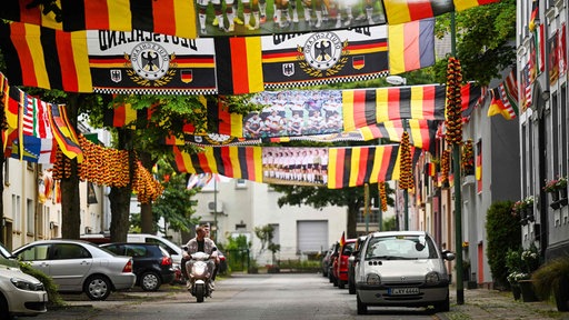 Vespa fährt durch mit Deutschlandflaggen geschmückte Straße