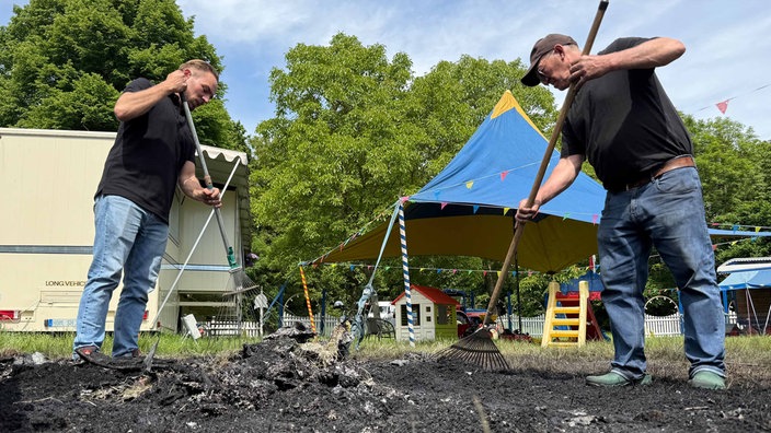 Zwei Männer kehren Aschereste zusammen.