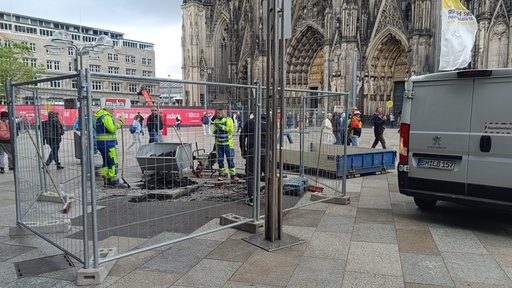 Auf der Kölner Domplatte parkt ein Baustellenfahrzeug und Bereiche sind mit Gitterzäunen für Bauarbeiten abgesperrt.
