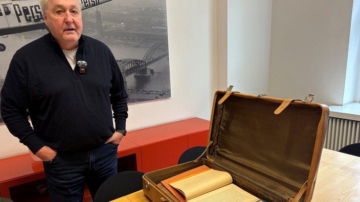 Autor Axel Spilcker steht neben dem Koffer mit Dokumenten seiner Familiengeschichte