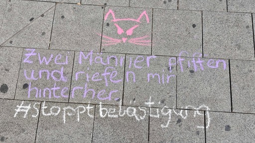 Auf Bordsteinen steht eine Kreidezeichnung zu Catcalling.