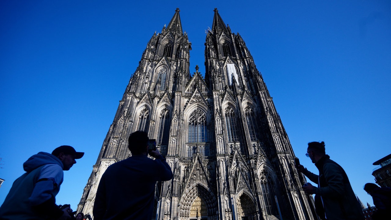 Der Kölner Dom vor blauem Himmel mit Besuchern davor.