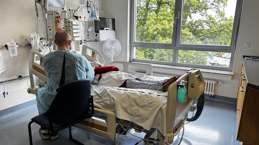 Mann sitzt an einem Krankenhausbett