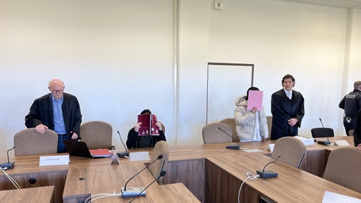 Zwei Angeklagte und Rechtsvertreter im Gerichtssaal.