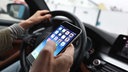 Ein Autofahrer hält während der Fahrt ein Smartphone in der Hand