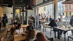 Auf dem Bild sieht man eine Gruppe von Menschen in einem Lokal sitzend, sie unterhalten sich 