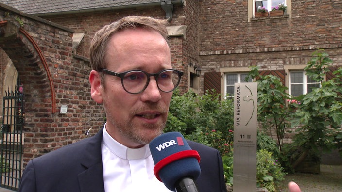 Pfarrer Herzberg vor rustikaler Kirche