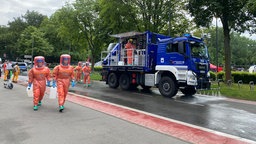 Menschen in Schutzanzügen während der Katastrophenschutzübung laufen neben einem Transporter