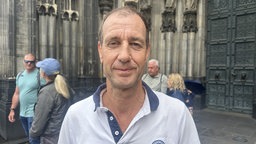 Ein Mann in weißem Shirt steht vor dem Kölner Dom