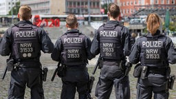 Mehrere Polizisten nebeneinander auf einem Platz, von hinten aufgenommen.