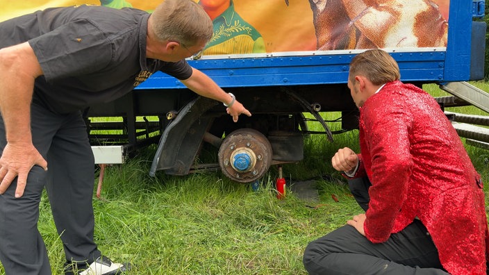 Zwei Männer hocken vor dem beschädigten Fahrgestell eines Lkw-Anhängers.