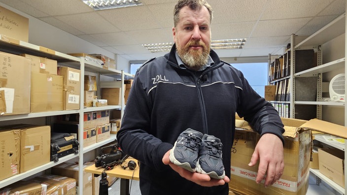 Zollbeamter (Jens Ahland)  hält Schuhe in die Kamera