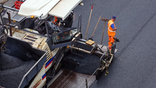 Ein Bauaerbeiter steht auf einem Asphaltfertiger 