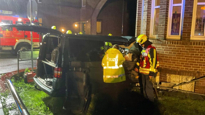 Ein Multivan ist in eine Hauswand gekracht. Polizei und Feuerwehr begutachten den Unfallwagen. 