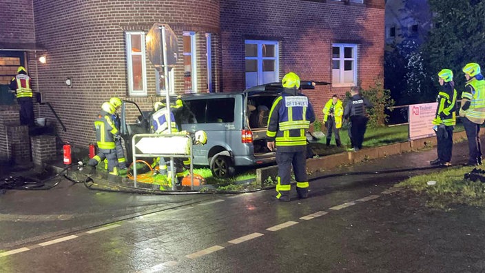 Ein Multivan ist in eine Hauswand gekracht. Polizei und Feuerwehr sichern den Unfallort. 