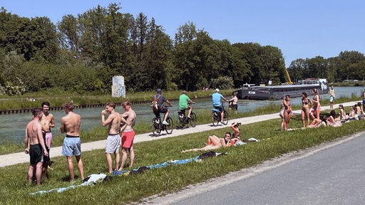 Dortmund-Ems-Kanal: ein Frachtschiff fährt vorbei und junge Menschen liegen in Badekleidung auf der Wiese