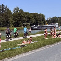 Dortmund-Ems-Kanal: ein Frachtschiff fährt vorbei und junge Menschen liegen in Badekleidung auf der Wiese