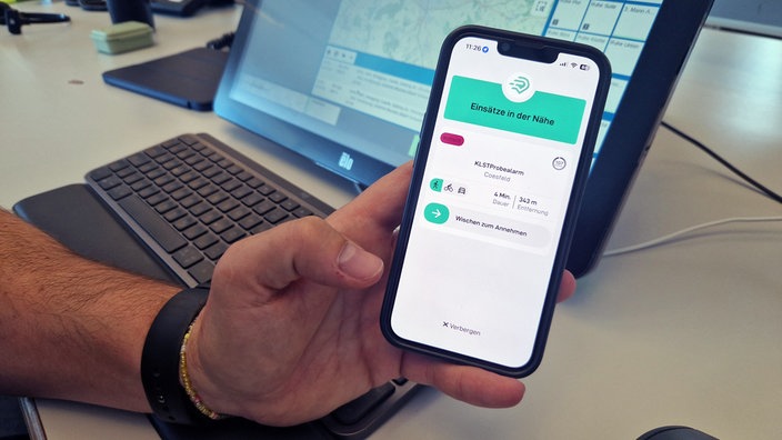 Ein Mensch hat ein Handy in der Hand und führt die Ersthelfer-App vor.