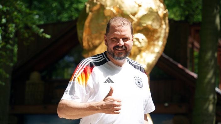 Toddy Geldmann steht glücklich vor dem großen WM-Pokal mit Daumen hoch.