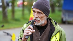 Ein Mann mit gelber Weste und Mütze spricht in ein Mikrofon.