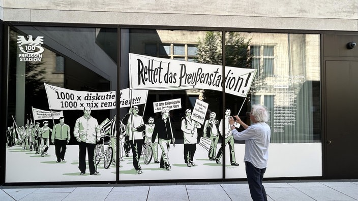 Fensterscheibe mit Illustration eines Streiks, auf den Schildern steht "Rettet das Preußenstadion" und "1000x diskutiert 10000x nix renoviert"