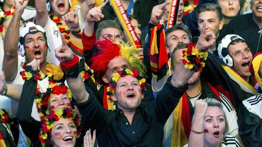 Ausschnitt von einer jubelnden Menge an Menschen beim Public Viewing. Alle tragen deutsche Fußball-Fanartikel wie Fußballtrikots oder Blumenketten in schwarz, rot, gelb.
