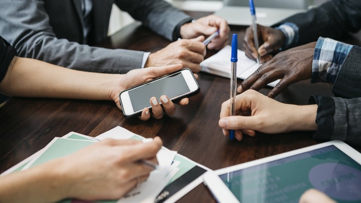 Die Händ von vier Personen auf einem Tisch mit Handy und Blöcken.