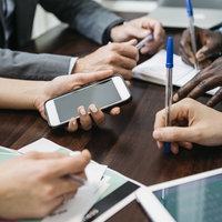 Die Händ von vier Personen auf einem Tisch mit Handy und Blöcken.