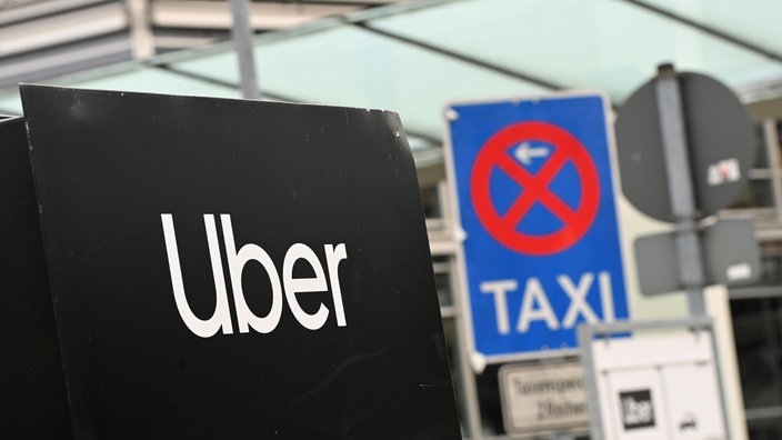 Ein Uber-Schild hebt sich gegen ein Schild für einen Taxistand ab.