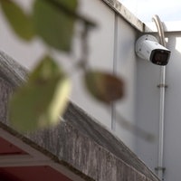 Auf dem Bild ist die Außenfassade einer Schule zu sehen. In einer Ecke unter dem Dach hängt eine Überwachungskamera.
