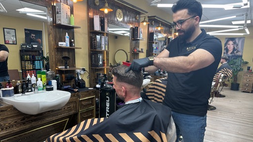 Friseur Mido steht in seinem Laden in Gronau-Epe und schneidet einem Kunden die Haare.