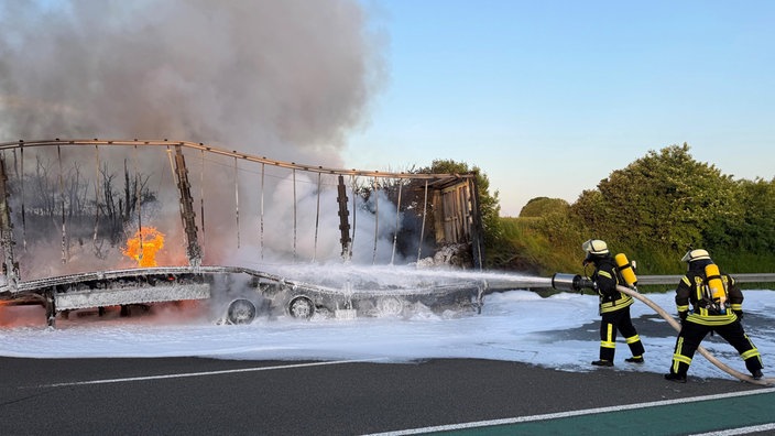 Ein ausgebrannter LKW-Auflieger und zwei Feuerwehrmänner, die noch löschen.