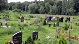 Muslimischer Friedhof mit Grabsteinen, im hintergrund Muslime an einem Grab